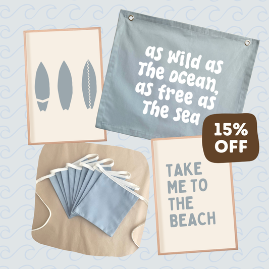 A collage-style product graphic showing beach-themed printed items: a light blue fabric banner with white text reading 'as Wild as The ocean, as free as The sea,' a cream print with gray surfboard silhouettes, a beige cloth with matching blue face masks, and a cream print with the phrase 'TAKE ME TO THE BEACH.' A brown badge says '15% OFF.