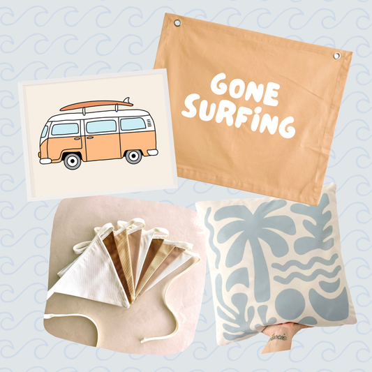 A collage of beach-themed home and apparel items on a pale blue patterned background: a tan fabric pouch with the words “GONE SURFING,” a cream card with a retro orange-and-white van illustration, folded white and tan fabric pieces, and a cream pillow with a light blue palm tree and wave print. A small tattooed hand is visible holding the pillow.