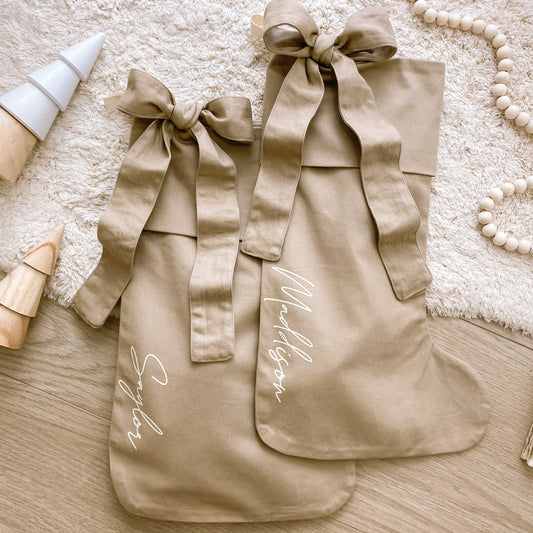 Personalised Christmas canvas bow stocking. Custom Christmas neutral stocking with bow. Minimalist bow Christmas stocking. Bow Name Christmas stocking. Personalised tan stocking with bow. Personalised cotton neutral bow stocking.