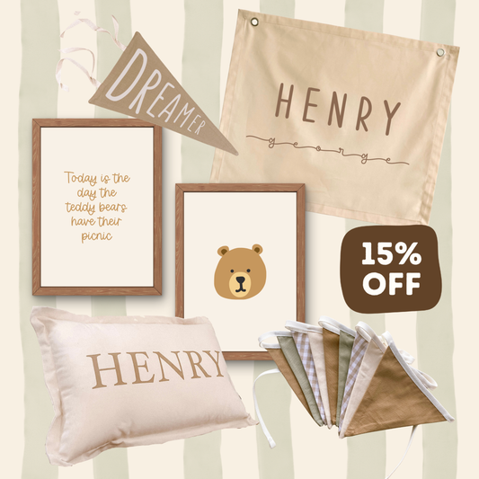 A coordinated nursery decor set featuring a personalized canvas wall banner reading 'HENRY', a framed quote print, a bear-face framed print, a pillow with 'HENRY' text, a folded fabric set, and a '15% OFF' badge on a cream striped background.