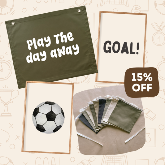 A promotional collage showing several framed sports-themed wall art prints and fabric flag samples on a beige background with faint sport icons. Visible items include a dark olive green flag reading 'Play the day away,' a cream print reading 'GOAL!,' a cream print with a soccer ball illustration, a stack of fabric flags, and a brown badge that says '15% OFF.
